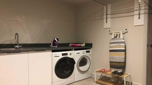 A compact kitchen with a washing machine, a sink, and a drying rack. - 4 Bed in Porth (oc-b584252) (Newquay)