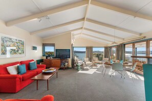 A spacious living area with a red sofa, a television, and a dining table with chairs. - Rainbow Point Yacht Club - Taupo Holiday Home (Taupo)