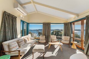 A sunlit room with a sofa, chairs, and a view of a lake. - Rainbow Point Yacht Club - Taupo Holiday Home (Taupo)