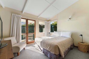 Ein Schlafzimmer mit Bett, Sessel, Schreibtisch, Lampe und einem Fenster mit Vorhängen.
