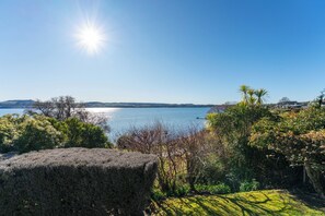 Klarer Blick auf einen See mit einer fernen Uferlinie, umgeben von dichter Vegetation und einer Steinstruktur im Vordergrund.