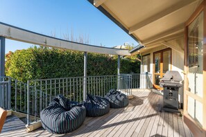 Eine überdachte Terrasse im Freien mit Grill, Sitzgelegenheit und Blick auf einen Heckenstreifen.
