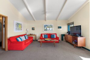 Ein Wohnzimmer mit zwei roten Sofas, einem Couchtisch, einem Fernseher und Bildern an den Wänden.