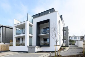 Un immeuble résidentiel moderne à deux étages, doté d’un toit plat, de grandes fenêtres et d’une porte de garage bien visible.