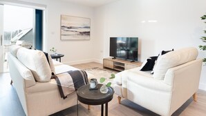 A modern living room with a sofa, a coffee table, a TV, and a painting on the wall. - 2 Bed in Falmouth (oc-b669230) (Flushing)