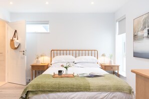 Une chambre moderne avec un lit en bois, des tables de chevet avec des lampes, un plaid vert et une fenêtre donnant sur un beau paysage.