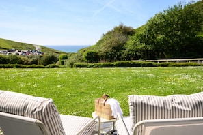 Eine grüne Außengelände mit Blick auf das Meer, umgeben von Hecken und Bäumen.