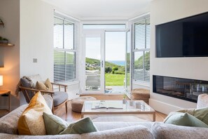 A modern living room with a sofa, armchair, and coffee table. There is a fireplace and a TV mounted on the wall. - 2 Bed in Watergate Bay (oc-b584254) (Tregurrian)