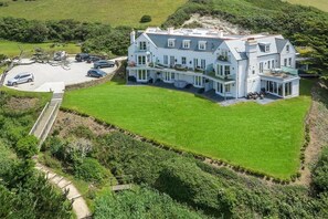 A large, two-story house with a spacious lawn, a driveway, and a small parking area. - 2 Bed in Watergate Bay (oc-b584254) (Tregurrian)