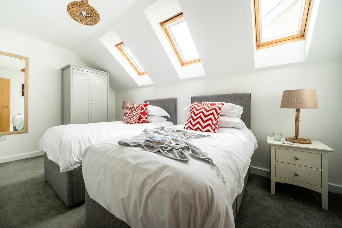 A bedroom with two beds, a wardrobe, a bedside table with a lamp, and skylights.