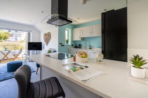 Eine moderne Küche mit einer großen Kochinsel, einem Flachbildfernseher und einem Essbereich mit einem blauen Sofa und einem Sessel.