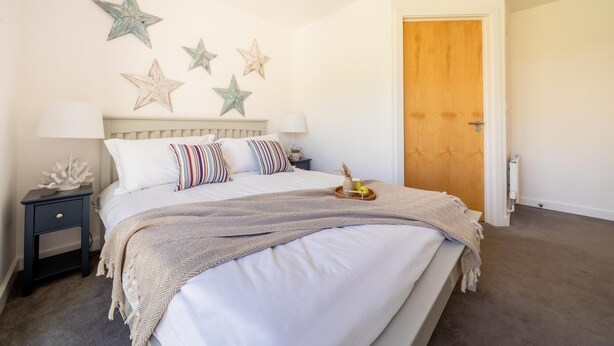 A bedroom with a bed, bedside tables, a wooden door, and decorative star wall art. - 2 Bed in Porth (oc-b588797) (Newquay)