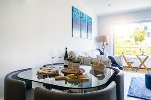 A modern living room with a glass-top dining table, a sofa, and a view of the outdoors. - 2 Bed in Porth (oc-b588797) (Newquay)
