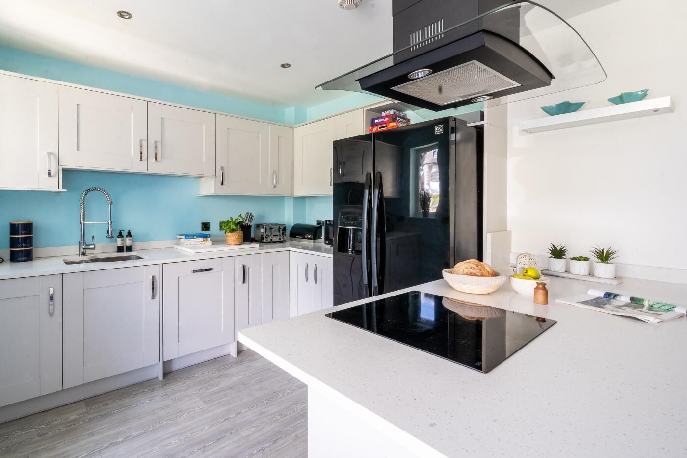 A modern kitchen with white cabinets, a black refrigerator, and a central island with a bowl of bread.