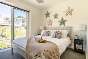 A bedroom with a large bed, a bedside table with a lamp, and a view of the outside. - 2 Bed in Porth (oc-b588797) (Newquay)