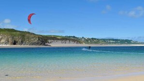A beach with clear water, a person windsurfing, and a red kite. - 3 Bed in Hayle (oc-b584309) (Hayle)