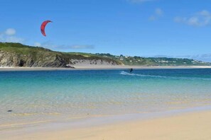 A beach with clear water, a person windsurfing, and a red kite. - 3 Bed in Hayle (oc-b584309) (Hayle)