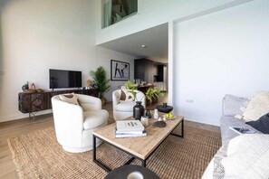 Een moderne woonkamer met een bank, fauteuils, een salontafel en een televisie.