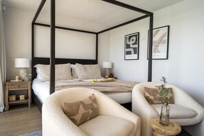 Een slaapkamer met een hemelbed, twee nachtkastjes, een stoel en een tafeltje met een vaas.