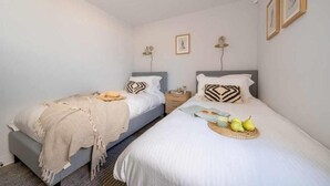 A bedroom with two beds, each with a headboard, a bedside table, and a lamp. - 3 Bed in Hayle (oc-b584309) (Hayle)