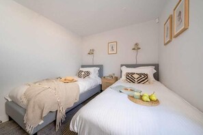 A bedroom with two beds, each with a headboard, a bedside table, and a lamp. - 3 Bed in Hayle (oc-b584309) (Hayle)