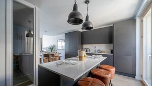 A modern kitchen with a central island, bar stools, pendant lighting, and a view into the dining area. - 3 Bed in Hayle (oc-b584309) (Hayle)