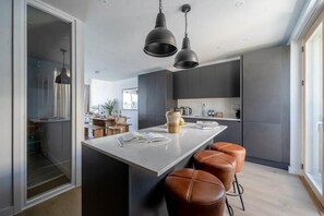 A modern kitchen with a central island, bar stools, pendant lighting, and a view into the dining area. - 3 Bed in Hayle (oc-b584309) (Hayle)