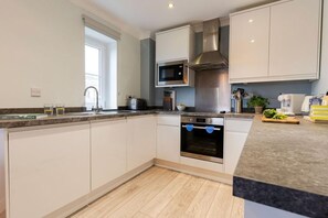 A modern kitchen with white cabinets, a stainless steel range hood, a built-in microwave, and a double oven. - 2 Bed in Watergate Bay (oc-b590010) (Watergate Bay)
