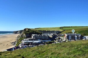 A coastal hotel with multiple buildings, a beach, and a hilly landscape. - 2 Bed in Watergate Bay (oc-b590010) (Watergate Bay)