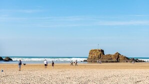 Een strand met mensen die wandelen en een grote rotsformatie in de verte.