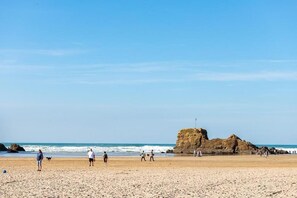 Ein Strand mit Menschen, die spazieren gehen, und einer großen Felsformation in der Ferne.