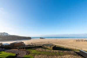 A beach with a wooden walkway and a building in the foreground. - 3 Bed in Perranporth (oc-b584315) (Perranporth)
