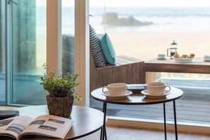 Ein gemütlicher Leseplatz mit Blick auf den Strand, ein kleiner Tisch mit Tassen und ein Blumentopf.