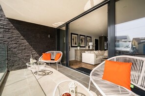 A modern living area with a stone wall, a glass door leading to a balcony, and a sofa with orange cushions. - 2 Bed in Bude (oc-b588786) (Bude)