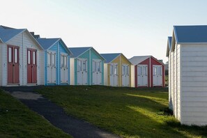 A row of beach huts with doors, a grassy area, and a path leading to them. - 2 Bed in Bude (oc-b588786) (Bude)