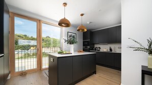 A modern kitchen with a central island, dark cabinetry, and pendant lighting. - 3 Bed in Hayle (oc-b624277) (Hele)