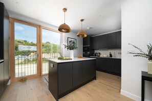 A modern kitchen with a central island, dark cabinetry, and pendant lighting. - 3 Bed in Hayle (oc-b624277) (Hele)
