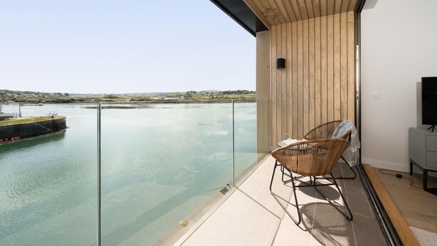 A balcony with a view of a calm body of water, a wicker chair, and a television on a cabinet. - 3 Bed in Hayle (oc-b624277) (Hele)