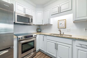 A modern kitchen with white cabinets, stainless steel appliances, and a granite countertop. - Phoenix VII #1509 -- New! 2BR Beachfront, Insane Gulf Views, Pool, Hot Tub, Gym (Orange Beach)