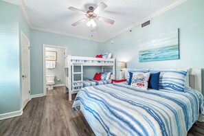 A bedroom with a bunk bed, a ceiling fan, a beach-themed wall art, and a wooden floor. - Phoenix VII #1509 -- New! 2BR Beachfront, Insane Gulf Views, Pool, Hot Tub, Gym (Orange Beach)