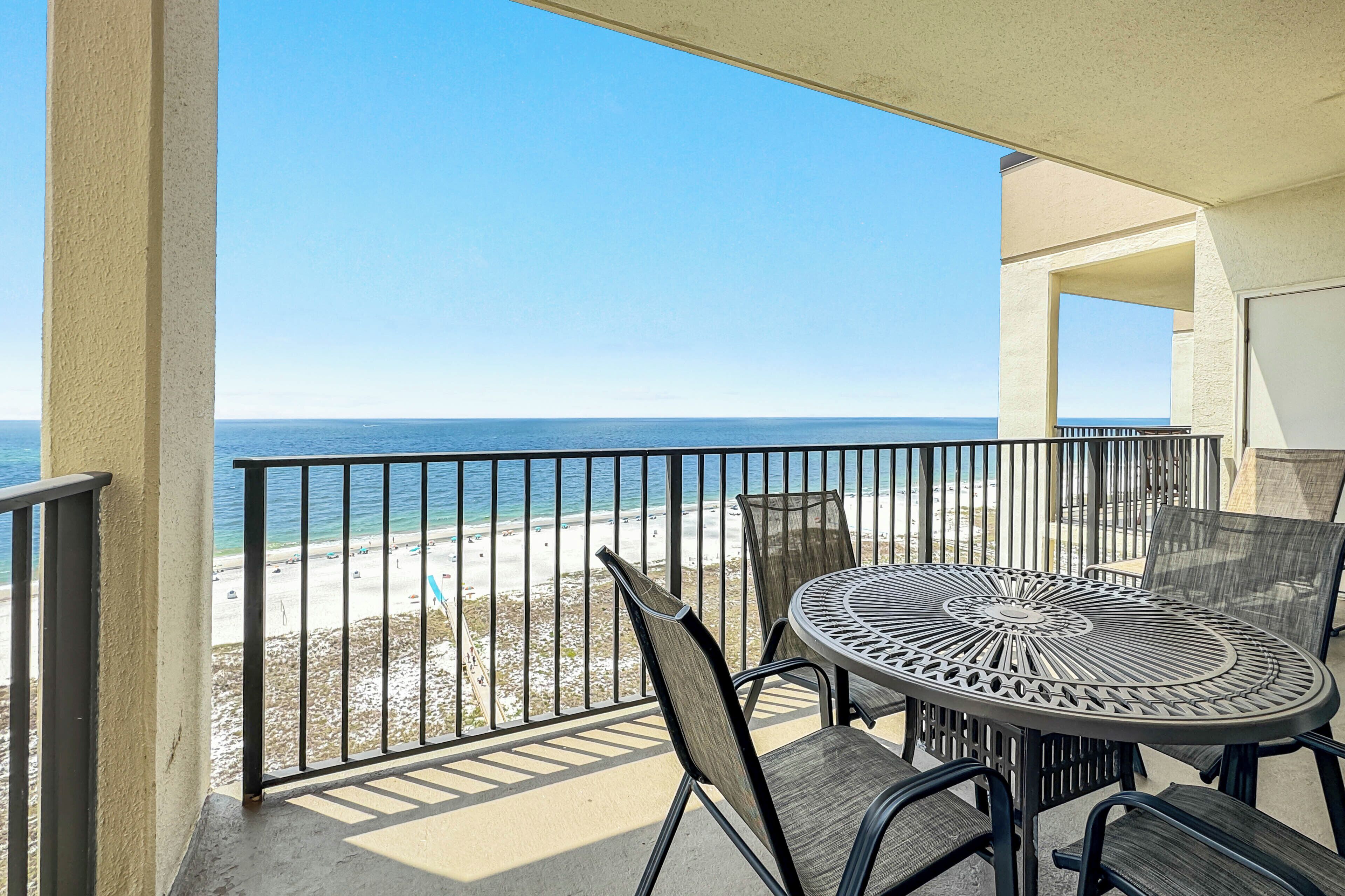 A balcony with a table and chairs overlooking a beach.