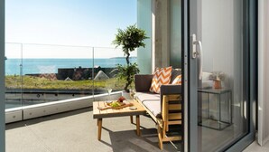 A balcony with a seating area, a table with fruits and a glass, and a view of the sea.