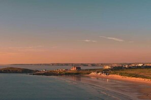 A coastal landscape with a beach, a lighthouse, and buildings in the distance. - 4 Bed in Fistral (oc-b584261) (Newquay)
