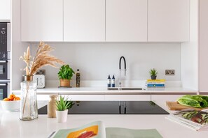 A modern kitchen with white cabinets, a black faucet, and a built-in dishwasher. - 4 Bed in Fistral (oc-b584261) (Newquay)