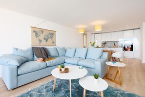 En moderne stue med en lyseblå sofa, to runde hvide borde, en blå måtte og et verdenskort på væggen.