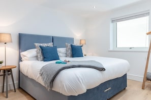 Ein modernes Schlafzimmer mit einem großen Bett, zwei Nachttischlampen und einem Fenster mit Jalousien.