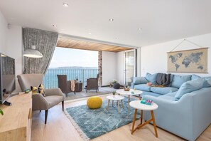 A modern living room with a sofa, chairs, a coffee table, and a view of the sea. - 3 Bed in Cawsand (oc-b584266) (Kingsand)