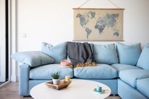 A light blue sofa with a world map on the wall behind it, a small round table with a plant and a cup, and a window to the left.