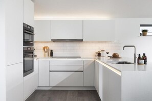 Eine moderne Küche mit weißen Schränken, einem eingebauten Ofen und einer Edelstahl-Spüle.
