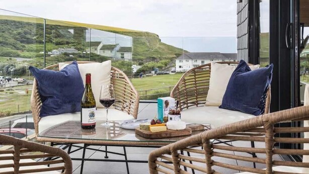 Ein Balkon mit Korbmöbeln, einem Glastisch und einer Weinflasche.